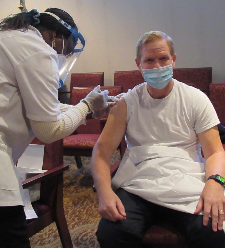 LSMMD's president and CEO getting sitting in a chair while getting the COVID-19 vaccination.