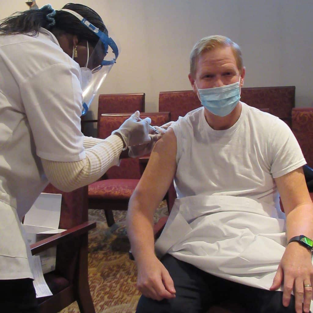 LSMMD's president and CEO, Jeff Branch, getting sitting in a chair while getting the COVID-19 vaccination.