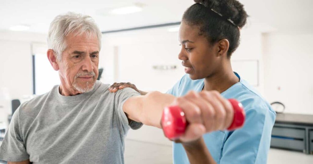 A physical therapist helping a senior man to do a lateral arm raise with a dumbell.