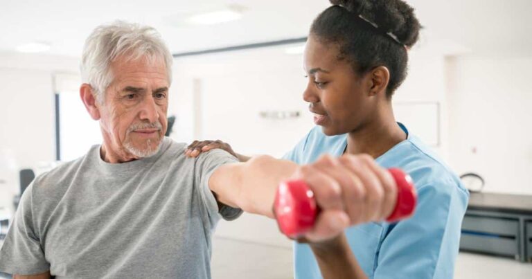 A physical therapist helping a senior man to do a lateral arm raise with a dumbell.