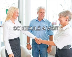 Photo of a sales counselor shaking hands with a senior couple while taking a tour and it states schedule a visit