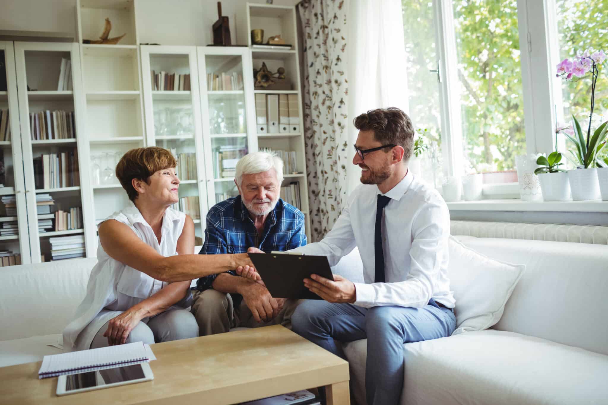 Photo of senior couple shaking hands and reviewing files with an advisor in a living room setting
