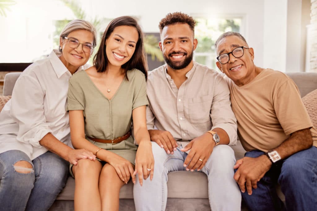 Adult children and their parents happily sitting on a couch after having a senior living conversation.