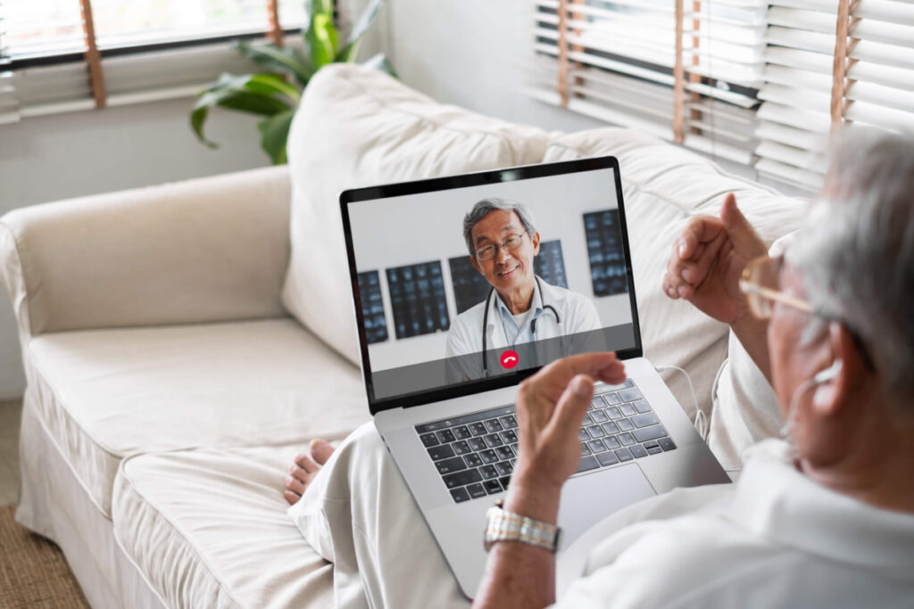 Older man with with laptop on a couch on a video conference managing personal safety for seniors.