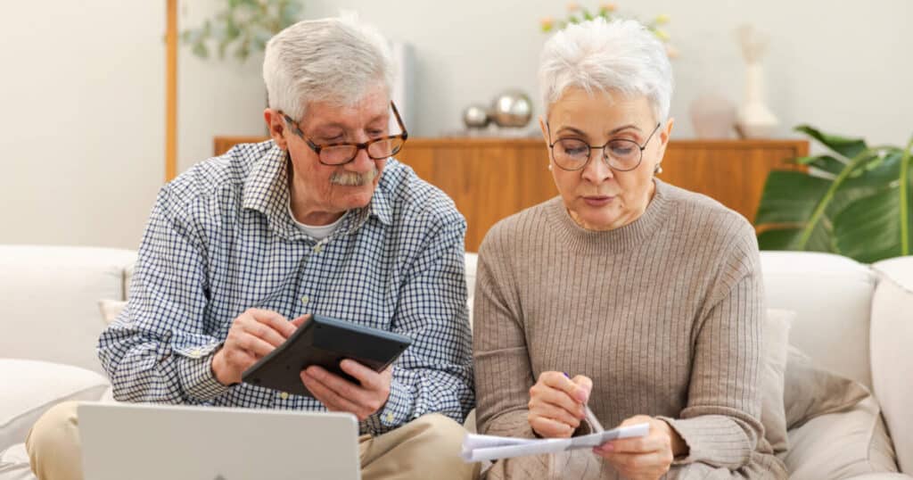 Elder couple on sofa reviewing finances Comparing Costs Can You Afford Active Adult