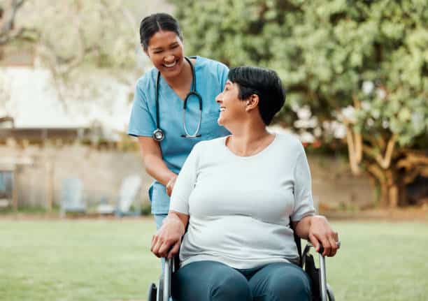 nurse pushes senior woman in a wheelchair through the park