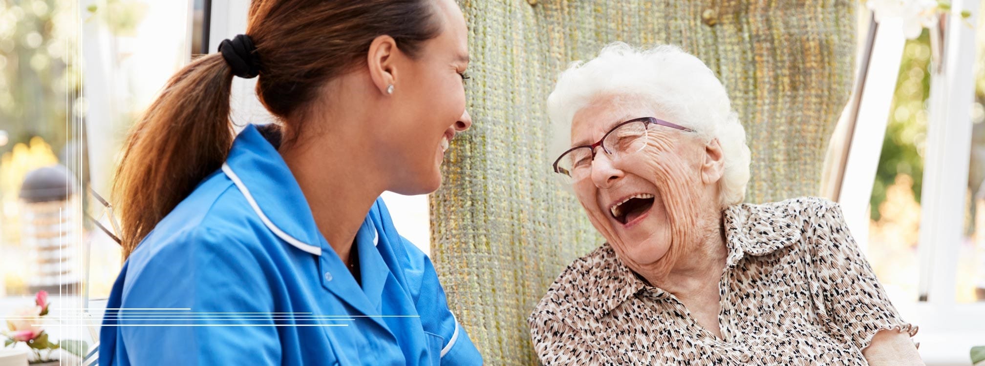 An assisted living memory care female resident laughing with a female dementia care professional team member.