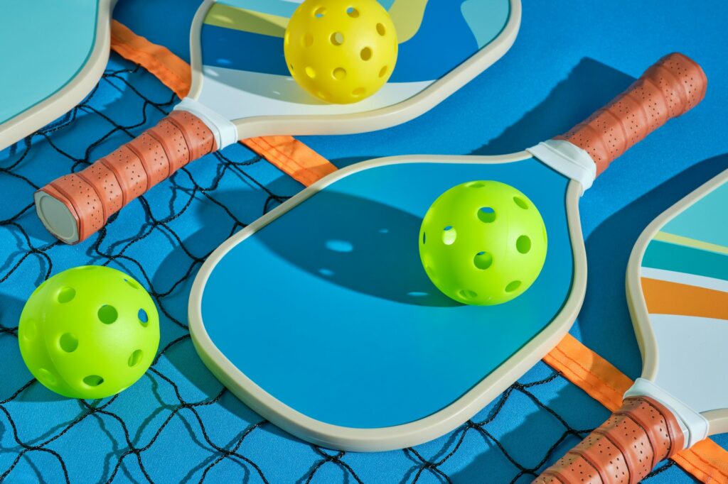 pickleball paddles with balls on top of a net on a blue background illuminated with hard light