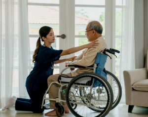 Caring nurse with senior man sitting on wheelchair at home.