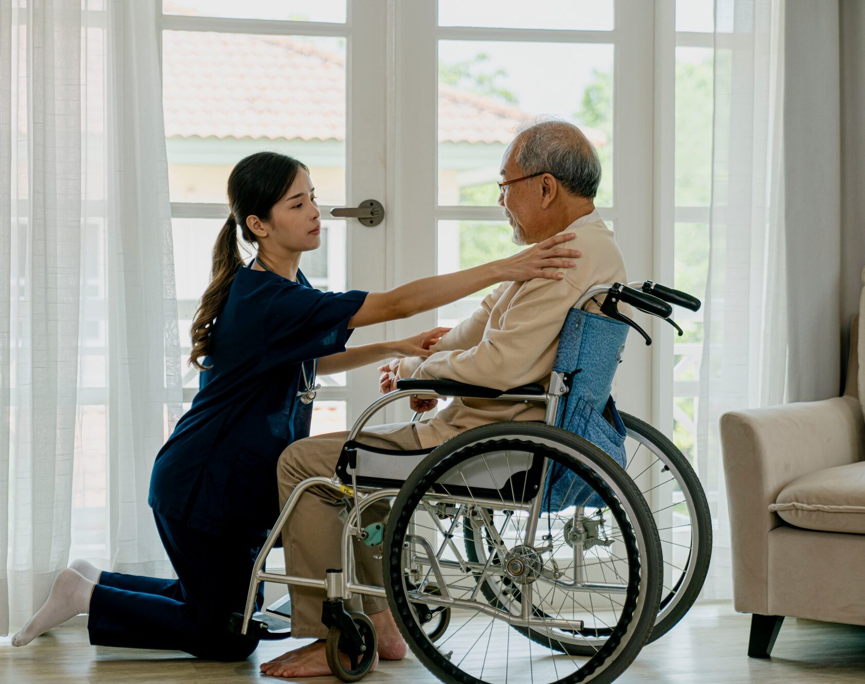 Caring nurse with senior man sitting on wheelchair at home.