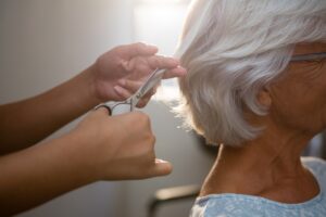 Cropped hands of beautician cutting hair of senior woman