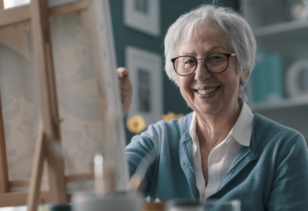 Happy elderly woman painting at home