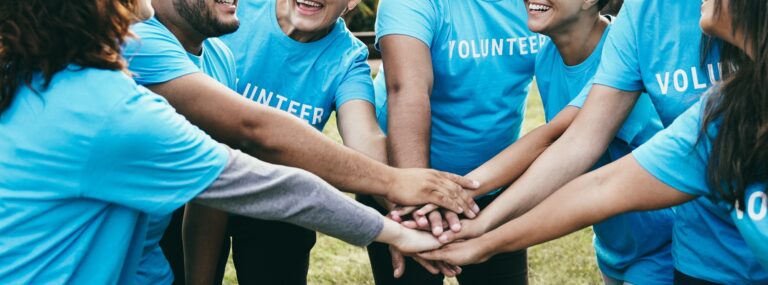 Happy group of volunteer people stacking hands celebrating together outdoor