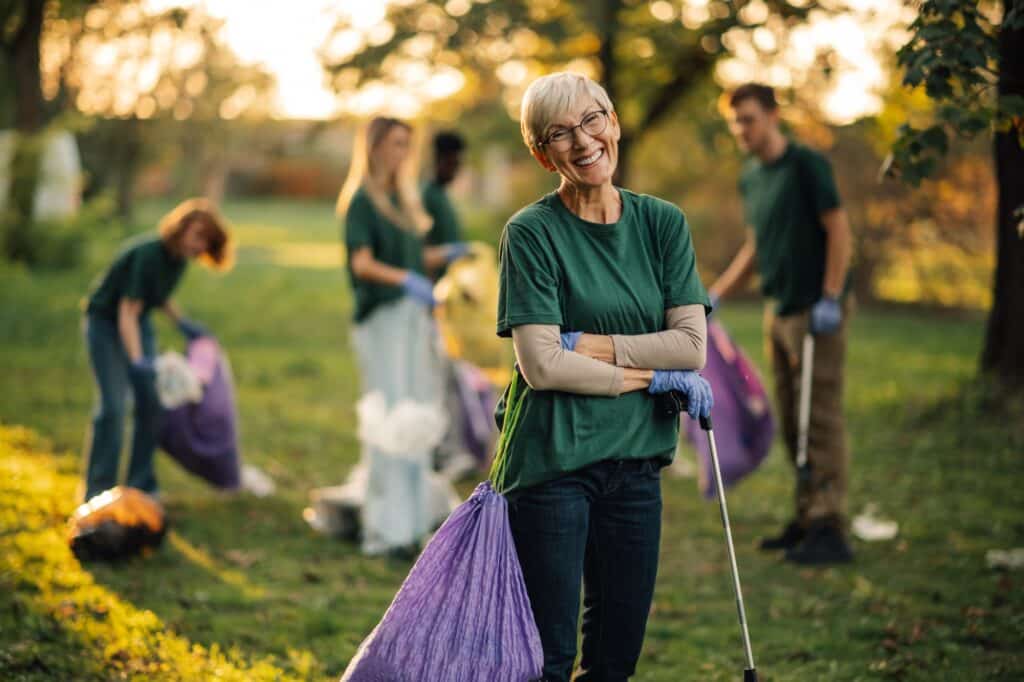 Happy senior volunteer posing while picking up trash in park