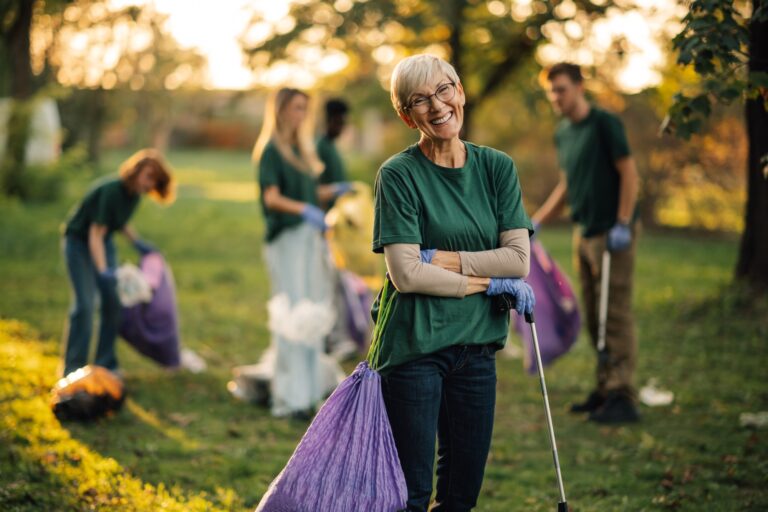 Happy senior volunteer posing while picking up trash in park
