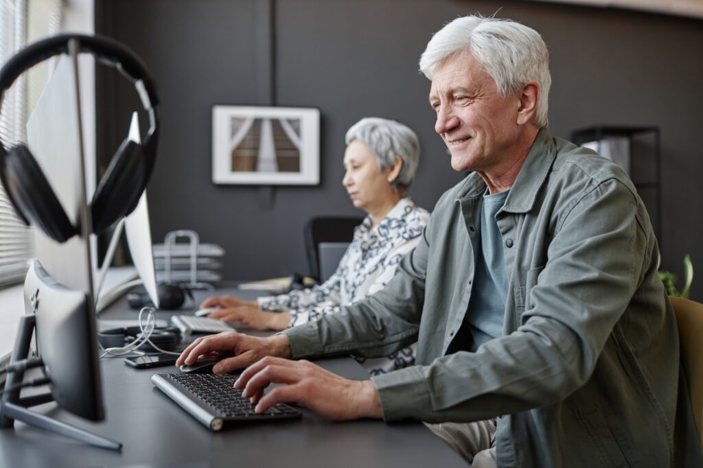 Smiling senior man using computer in class for elderly people
